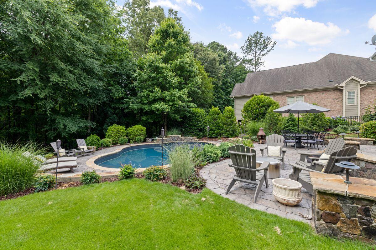 Landscaped backyard patio with Adirondack chairs, outdoor dining and a pool